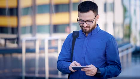 Cheerful-man-browsing-smartphone-at-office.-Smiling-bearded-office-worker-using-smartphone-at-office-building-on-the-street