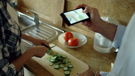 Atractiva-pareja-cocinar-en-la-cocina-y-tomar-fotos-utilizando-smartphone-fo-compartir-medios-de-comunicación-social-en-el-país