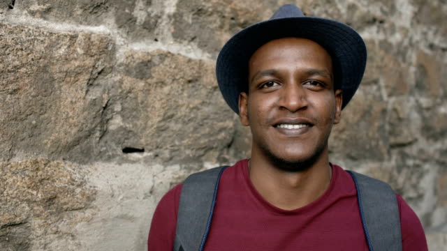 Portriat-of-happy-african-tourist-man-backpacker-smiling-and-looking-into-camera.-Mixed-race-young-guy-travelling-in-Europe