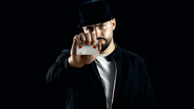 Professional-Straße-Zauberer-in-einer-Kappe-führt-durch-beeindruckende-Sleigth-von-Hand-Kartentrick.-Hintergrund-ist-schwarz.