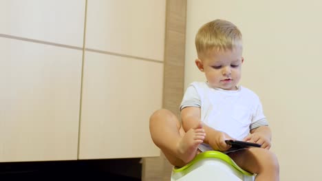 Cute-niño-pequeño-juega-con-teléfono-sentado-en-el-orinal