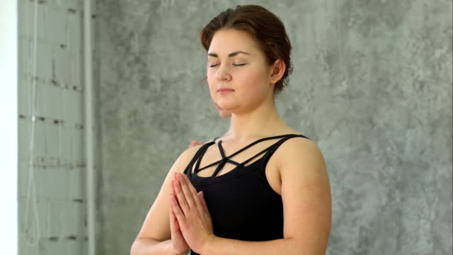 Portrait-of-young-beautiful-athletic-girl-practicing-indoor-yoga-with-closed-eyes-and-palms-in-namaste-gesture