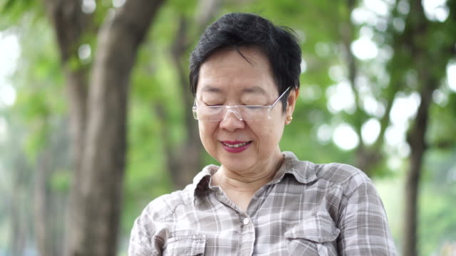 Asiatische-senior-Frau-sitzt-und-liest-ein-Buch-im-grünen-Naturpark-Hintergrund