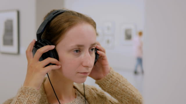 Mujer-busca-en-exposición-y-escuchar-a-audio-guía-en-fotos-modernas