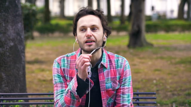 Hombre-encantador-hablar-por-teléfono-con-los-auriculares,-sentado-en-un-parque-en-el-Parque