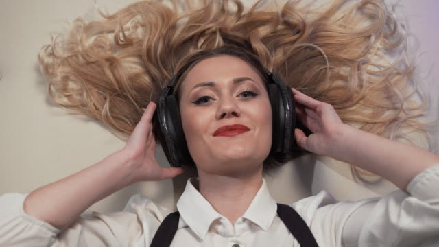 close-up-Woman-lying-on-the-bed,-listens-to-music-in-big-headphones-and-reacts-to-her-sexually-smiling