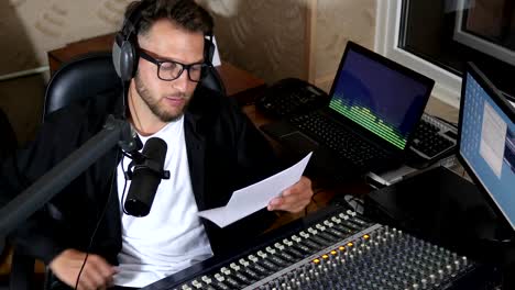 junger-Mann-in-Brille-und-Kopfhörer-liest-Text-ins-Mikrofon-während-der-Arbeit-im-radio