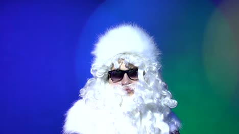 Santa-Claus-in-sunglasses-looking-at-the-camera-at-party.-Multicolored-lighting-background