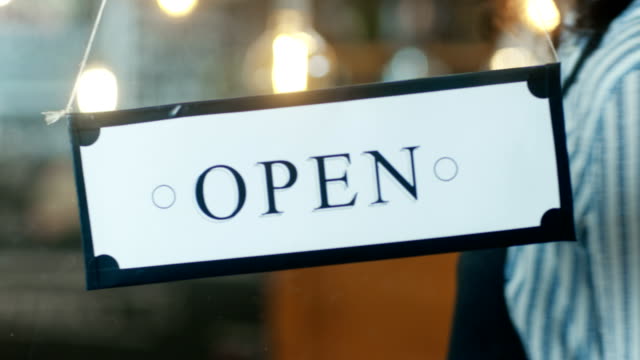Close-up-Shot-of-the-Woman-Hanging-Open-Sign-in-the-Storefront.