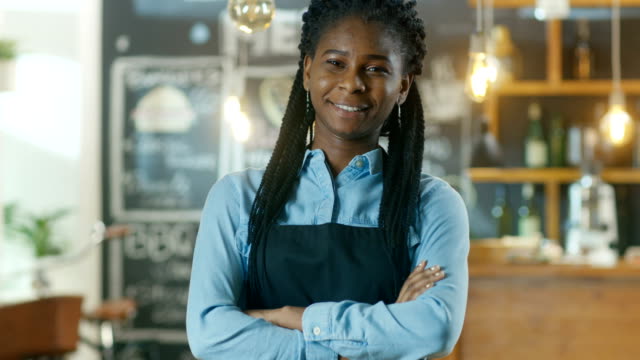 Schöne-African-American-Cafe-Besitzer-Stand-mit-verschränkten-Armen-und-einem-Lächeln-in-ihrem-stilvollen-Kaffeehaus.