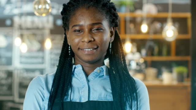 Schöne-African-American-Cafe-Besitzer-zu-Fuß-in-den-Vordergrund-in-den-Hintergrund-ihrer-stilvollen-Kaffee-Haus-glänzt-mit-Lichter.