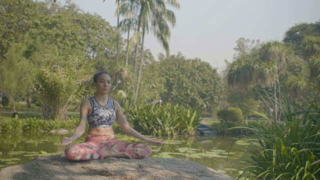 Junge-asiatische-Frau-Yoga-draußen-im-Park-machen.-Attraktive-Frau,-die-in-Lotus-Pose-im-schönen-Sonnenlicht-meditieren.
