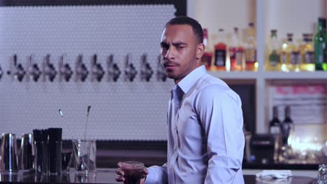 Portrait-shot-of-a-young-attractive-African-American-man-looking-at-the-camera-in-a-seious-manner-at-a-bar