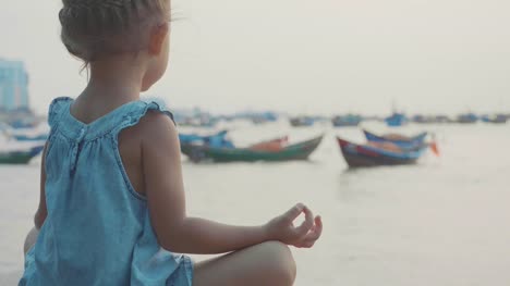 Kleine-süße-Mädchen-meditiert-in-türkischen-Pose-am-Meer