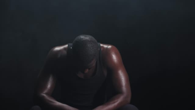 Zooming-shot-of-a-muscular-black-man-resting-in-between-workouts-on-a-foggy-dark-background