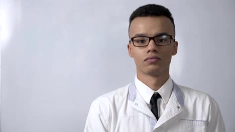 Yes-by-shaking-head,-gesture-by-young-successful-African-scientist-in-a-white-coat-and-glasses-looks-at-the-camera,-portrait-concept.-60-fps
