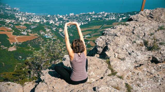 Sitting-woman-in-lotus-position-practicing-yoga-moves-or-meditates-and-Raises-her-arms-up-in-mountains