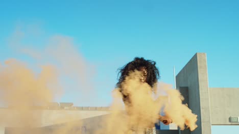 Young-woman-dancing-outside-with-smoke-grenade-at-sunset-on-rooftop-parking-garage