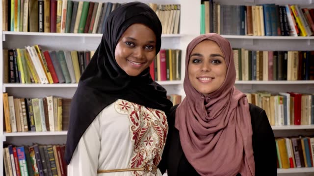 Portrait-of-two-charming-young-muslim-womens-standing-in-library-and-smiling-in-camera,-african-muslim-women-in-hijab