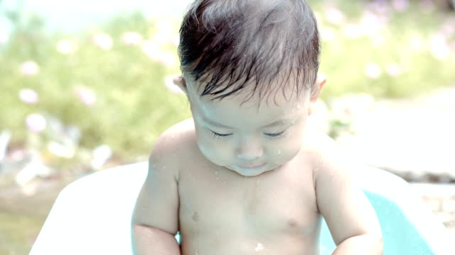 Asia-niño-7-meses-de-edad,-bañarse.-Tomo-baño-para-bebés.-Niño-tocando-el-agua-con-el-sol.-Diversión-acuática-para-niños