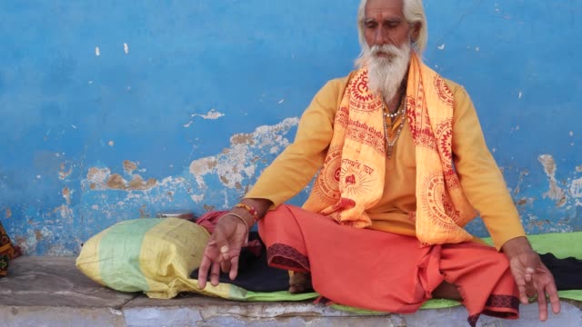Dolly-in-to-Sadhu,-Indian-saint,-sitting-outside-a-temple-in-meditation-against-a-blue-wall