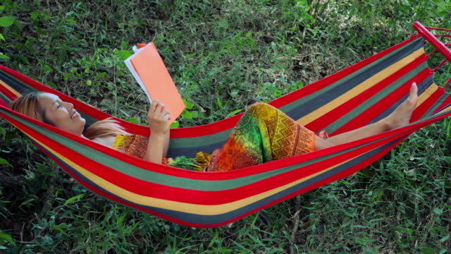 Young-woman-laying-down-on-hammock-and-reading-a-book