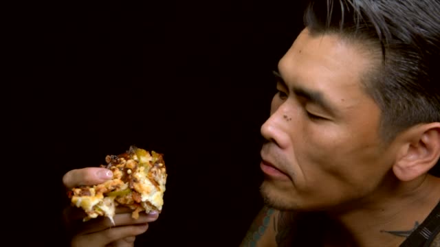 asiatische-tätowierter-Mann-isst-leidenschaftlich-gern-ein-Stück-pizza