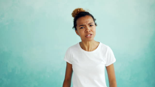 Portrait-of-angry-mixed-race-woman-talking-and-gesturing-expressing-negative-emotions-standing-against-light-blue-background.-Feelings-and-people-concept.