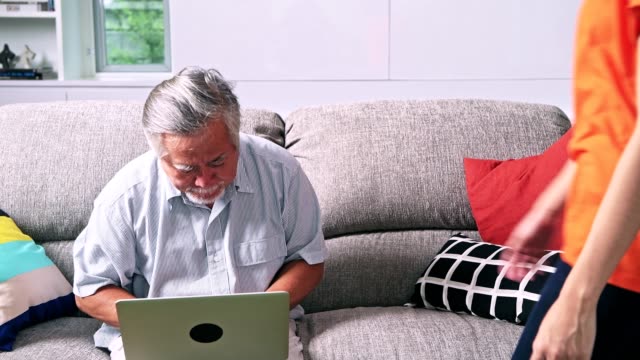 Tochter-Unterricht-ihres-Vaters-Computerkenntnisse-im-Wohnzimmer.-Asiatischer-Mann-mit-weißem-Bart-und-junge-Frau-sitzt-im-Wohnzimmer-mit-Laptop.-Familie-Senior-Lifestyle-Konzept.