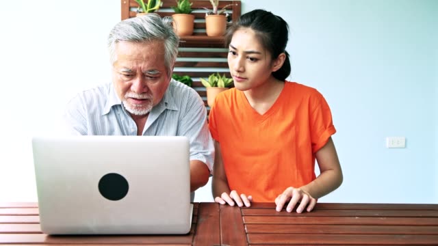 Daughter-teaching-her-father-computer-skills-in-balcony.-Asian-man-with-white-beard-and-young-woman-sitting-in-balcony-using-laptop.-Senior-lifestyle-family-concept.