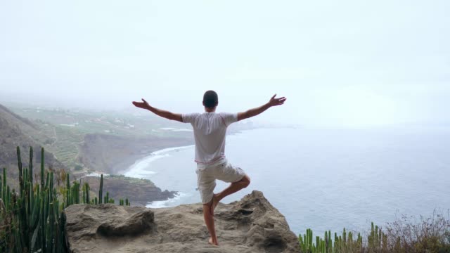 A-man-standing-on-one-hand-in-the-mountains-with-his-back-to-the-camera-looking-at-the-ocean-and-meditating-on-the-Canary-Islands.
