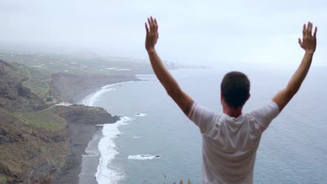 The-man-standing-on-the-edge-of-a-cliff-in-the-pose-of-the-dog-with-views-of-the-ocean,-breathe-in-the-sea-air-during-a-yoga-journey-through-the-Islands