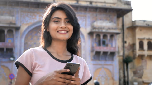An-attractive-girl-using-smartphone-or-cellphone-is-smiling-looking-at-the-camera