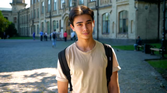 Nice-asian-male-is-looking-up-and-straight-after,-enjoying-summer-days,-being-near-great-old-buildings