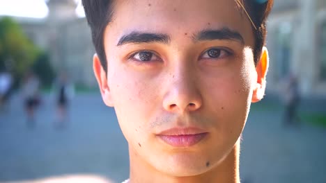 Close-up-portrait-of-asian-male-looking-at-camera-straight,-serious-concentrated-mood-in-shadow,-summer-outdoor