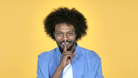 Afro-amerikanischer-Mann-gestikulierte-Stille,-Finger-auf-die-Lippen,-gelber-Hintergrund