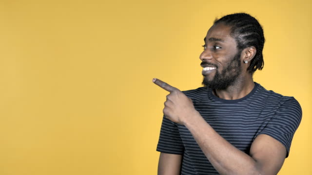 Casual-African-Man-Pointing-with-Finger-on-Side,-Yellow-Background