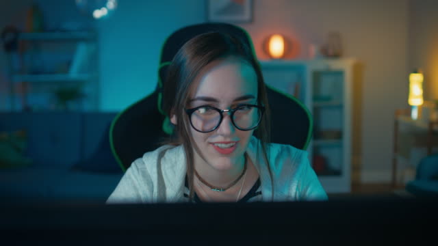 Excited-and-Pretty-Gamer-Girl-in-Glasses-is-Playing-Online-Video-Game-on-Her-Personal-Computer.-Room-and-PC-have-Colorful-Warm-Neon-Led-Lights.-Cozy-Evening-at-Home.