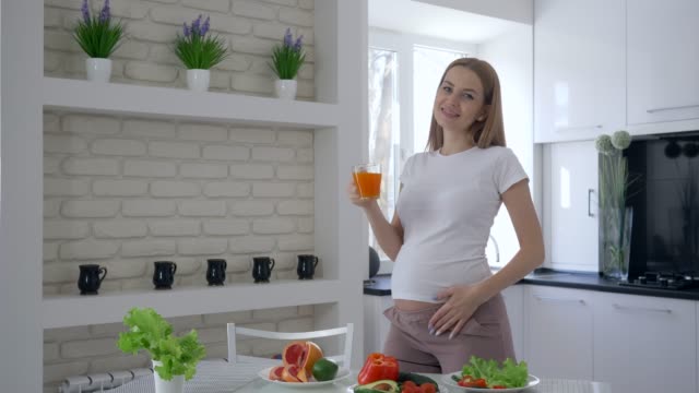 Vitamine-für-Schwangerschaft,-lächelt-glücklich-schwangere-Frau-mit-großen-Bauch-trinken-Saft-aus-frischen-Früchten-während-gesundes-Frühstück-in-der-Küche-im-Appartement