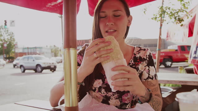 A-beautiful-girl-at-an-outdoor-table-eating-a-burrito,-slow-motion