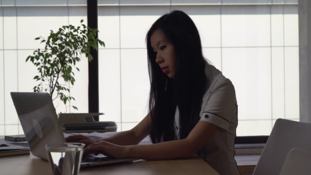 Empresaria-asiática-trabajando-en-la-oficina-moderna-en-el-fondo-grandes-ventanas