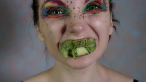 4k-Shot-of-a-Woman-with-Multicoloured-Make-up-Squeezing-a-Kiwi-in-Mouth