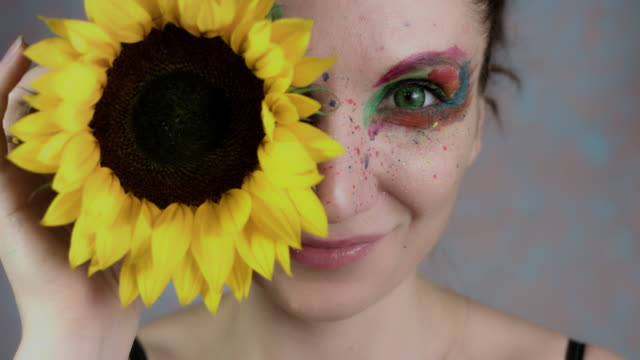 4k-Shot-of-a-Woman-with-Multicoloured-Make-up-With-Sunflower-(focus-on-eye)