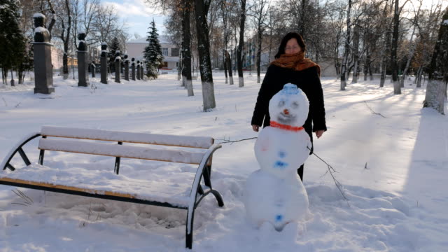 Joven-mujer-edificio-muñeco-de-nieve-en-el-parque.-En-el-invierno