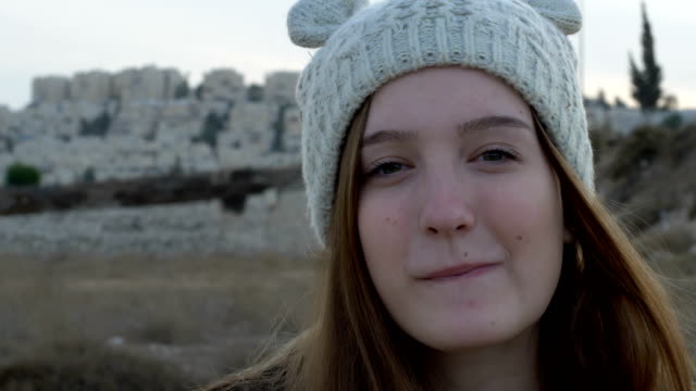 Porträt-eines-schönen-Mädchens-in-einer-gestrickten-Mütze,-die-zeigt-und-essen-israelische-Erdnuss-Snacks-Bamba,-im-Freien,-Lagermaterial.