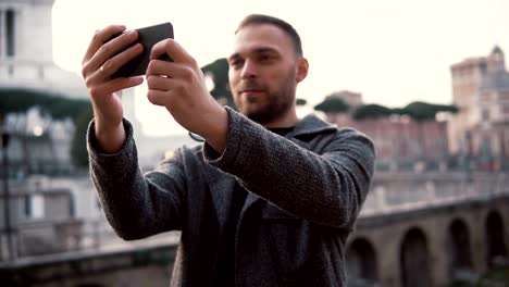 Man-tourist-explores-new-city,-takes-selfie-photos-of-city-centre-on-the-smartphone.-Male-enjoys-trip-to-Rome,-Italy