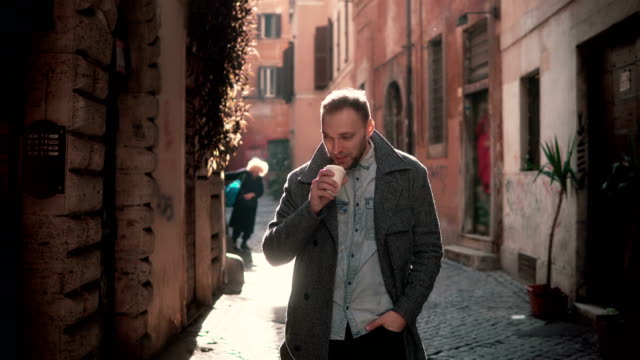 Portrait-of-young-handsome-man-looking-at-camera.-Happy-smiling-male-standing-in-morning-street,-drinking-coffee