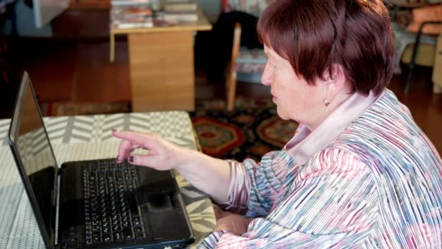 Una-mujer-mayor-comprueba-los-mensajes-en-las-redes-sociales-en-un-ordenador-portátil-en-casa.-Ella-se-sienta-en-la-mesa