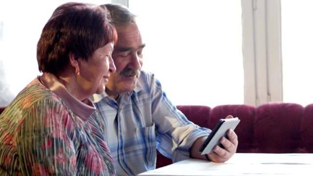 Una-pareja-de-ancianos-se-comunica-con-su-nieto-por-video-a-la-tableta.-Un-hombre-y-una-mujer-están-hablando-a-familiares
