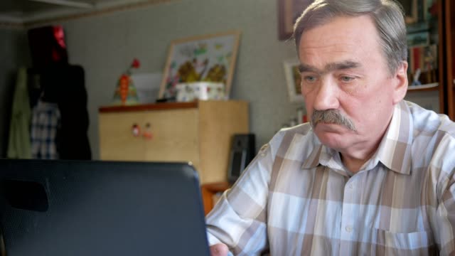 Ein-älterer-Mann-mit-einem-Schnurrbart-sitzt-hinter-einem-Laptop-und-löst-Probleme.-Er-schaut-ernst-auf-dem-monitor